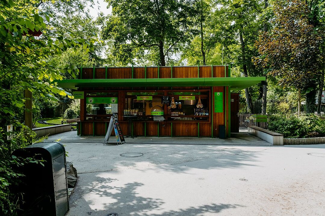 Der Kiosk Kinderland aus der Ferne. Ein grünes Vordach und zahlreiche Süßigkeiten sind zusehen.