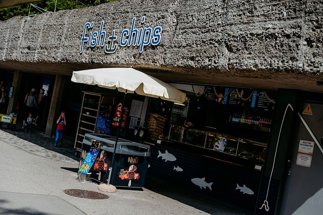 Sie Sonne scheint auf den Kiosk fish and chips. Davor steht ein Sonnenschirm und darunter eine Eistruhe.