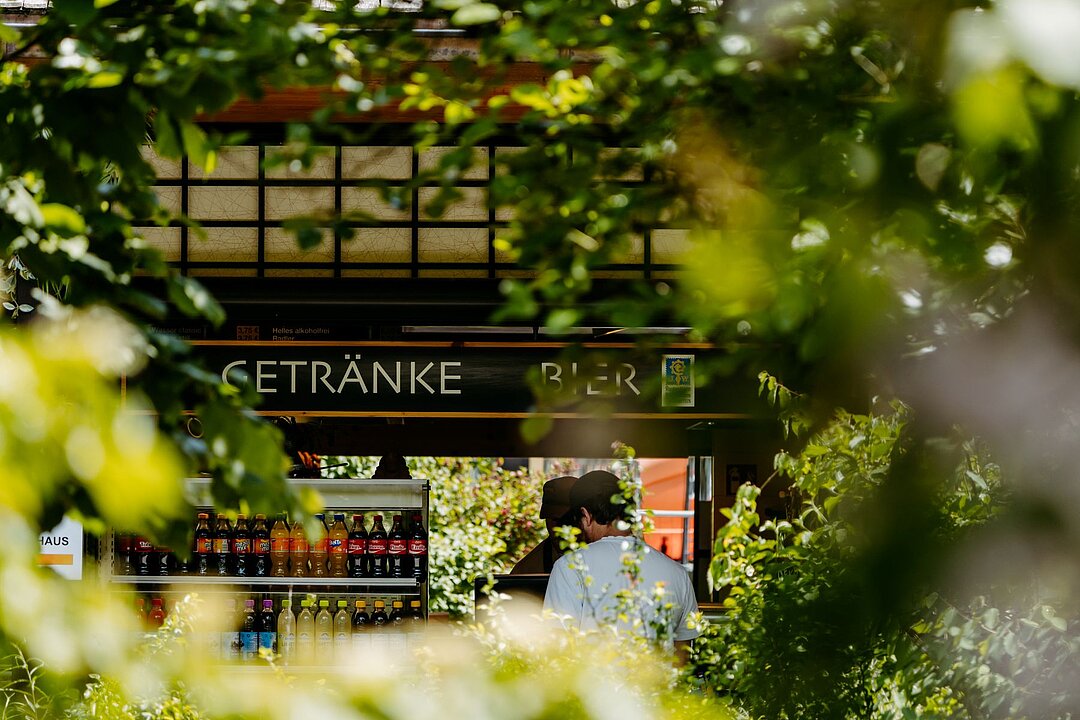 Der Tao Garten aus der Ferne. Durch Bäume hinweg sieht man die Getränkeausgabe.